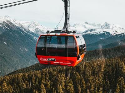 Rode gondel van Peak 2 Peak in Whistler Blackcomb boven bos en besneeuwde bergen in Canada.
