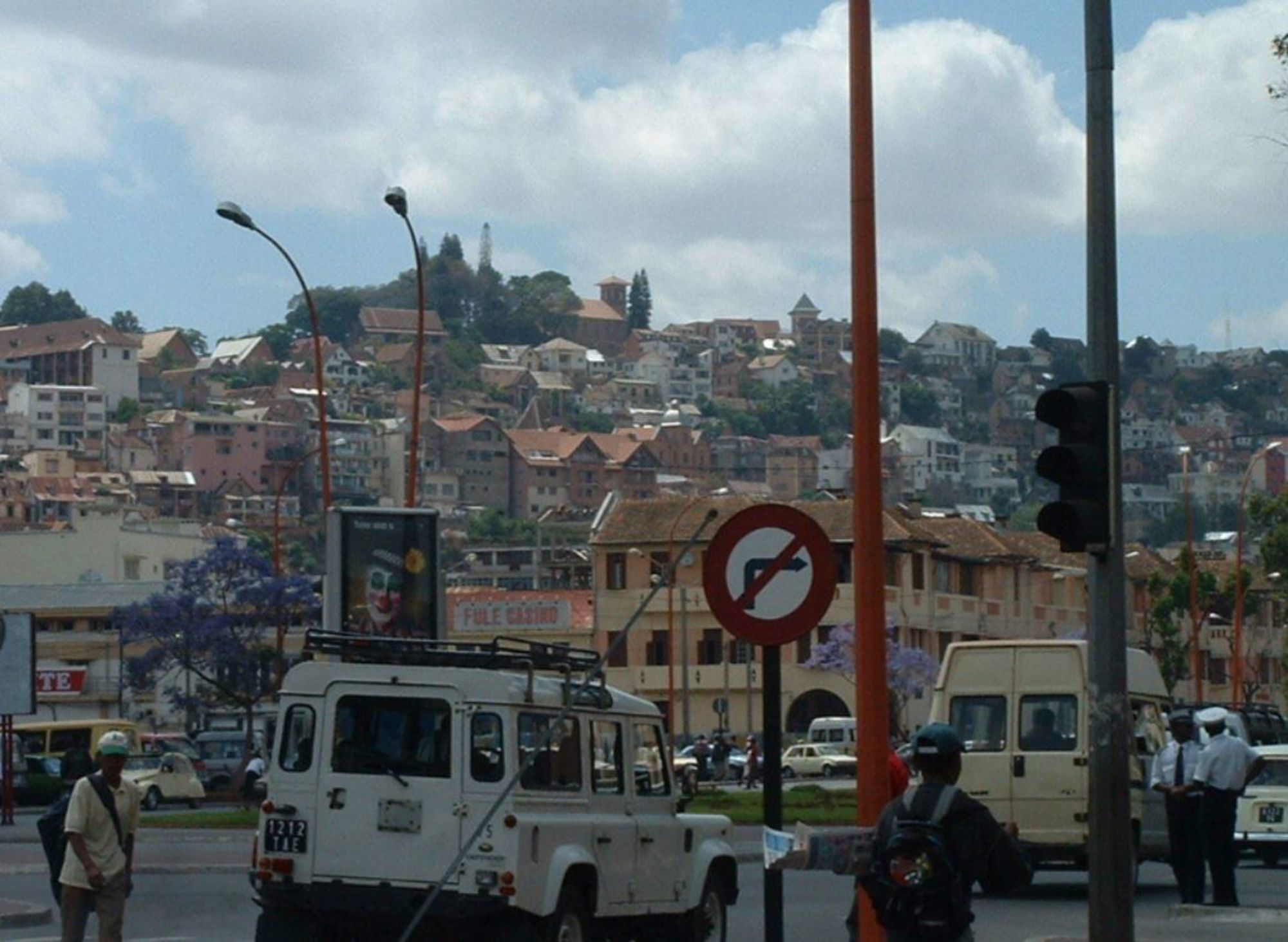 Straatbeeld in Antananarivo, Madagascar, met verkeer en huizen op een heuvel op de achtergrond.