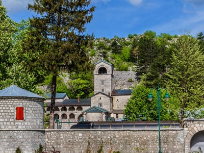 Kloostercomplex in de Balkan met stenen toren en kapel, omringd door groen en bergen.