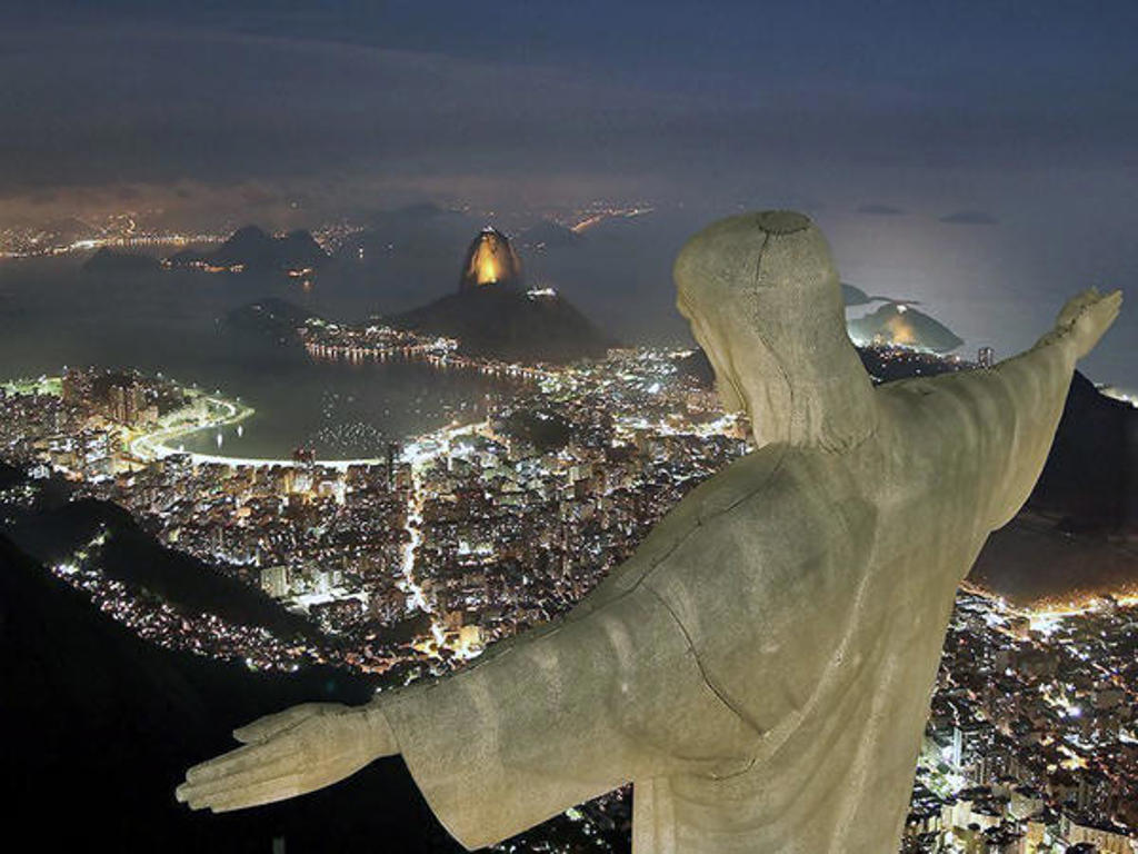 Christus de Verlosser kijkt uit over Rio de Janeiro bij nacht, met de Suikerbroodberg op de achtergrond.