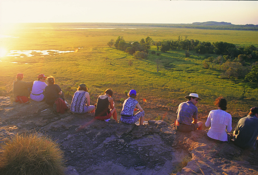 Reizigers kijken bij zonsondergang uit over de uitgestrekte outback tijdens een groepsrondreis door Australië.