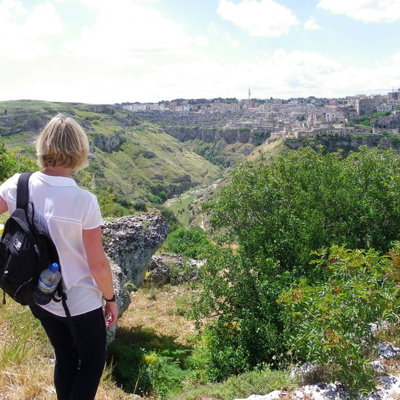 Wandelaar met rugzak kijkt uit over de ravijnvallei en het stadsgezicht van Matera, Italië.