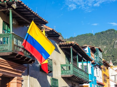 Colombiaanse vlag aan balkon van kleurrijke huizen in Bogotá, met groene bergen op de achtergrond.