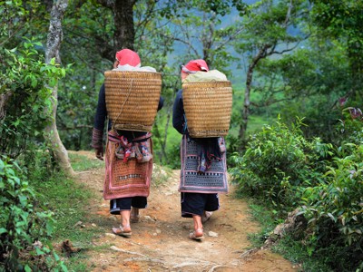 Twee vrouwen met rieten draagmanden wandelen over een bospad in de bergen van Vietnam tijdens de Route Vietnam.