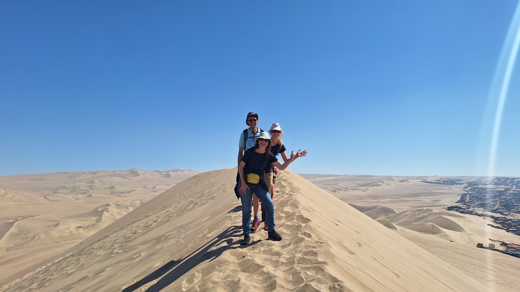 Gezin op een hoge zandduin tijdens familiereis Peru, met uitgestrekte woestijn op de achtergrond.