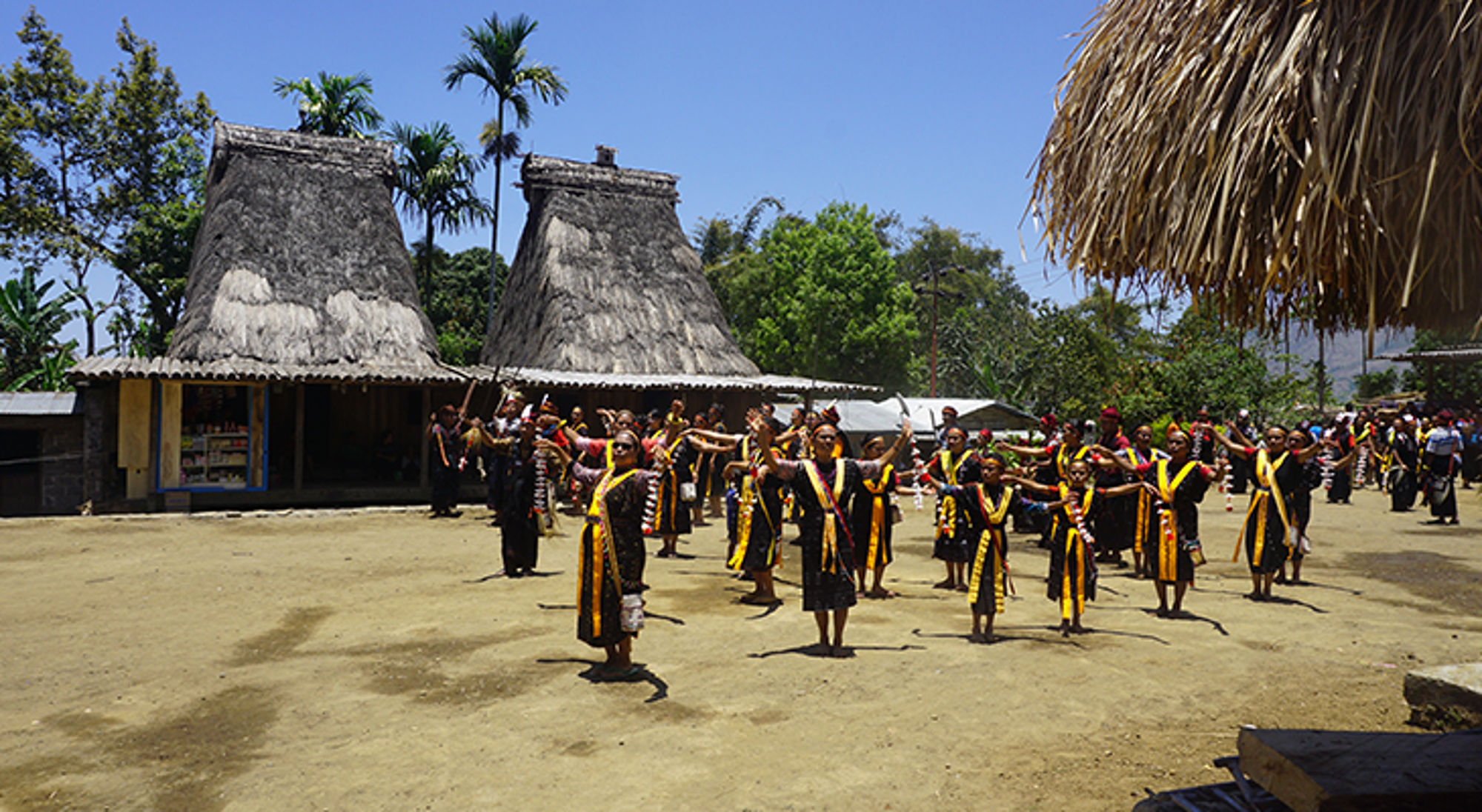 Traditionele dansvoorstelling in Indonesisch dorp met rieten huizen en dansers in kleurrijke kledij.