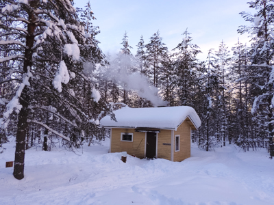 Houten sauna in besneeuwd bos in Lapland, met rook uit de schoorsteen.