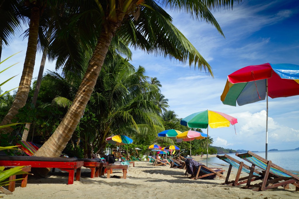 Palmenstrand met kleurrijke parasols en strandstoelen tijdens een familiereis door Thailand, Laos en Cambodja.