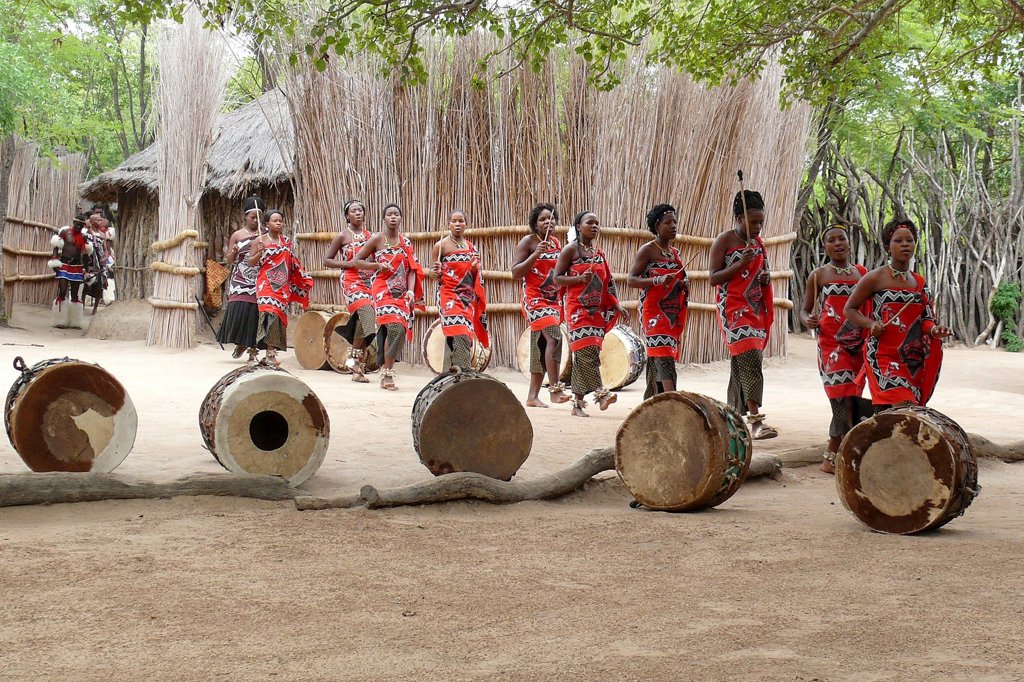 Dansers in kleurrijke kleding met trommels bij een traditioneel dorp in eSwatini tijdens een groepsrondreis.