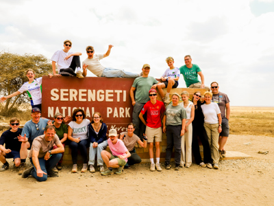 Familiegroep poseert bij het bord van Serengeti National Park tijdens familiereis Tanzania en Zanzibar.
