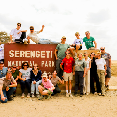 Familiegroep poseert bij het bord van Serengeti National Park tijdens familiereis Tanzania en Zanzibar.