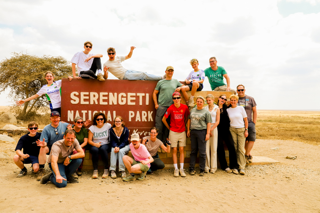 Familiegroep poseert bij het bord van Serengeti National Park tijdens familiereis Tanzania en Zanzibar.