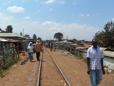 Spoorlijn door een woonwijk met voetgangers langs de rails, tijdens de route Kenia en Tanzania.