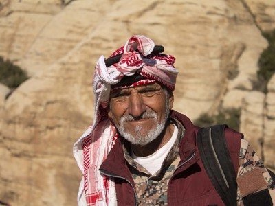 Portret van Jordaanse gids met rood-witte keffiyeh in rotsachtig woestijnlandschap tijdens route Jordanië.