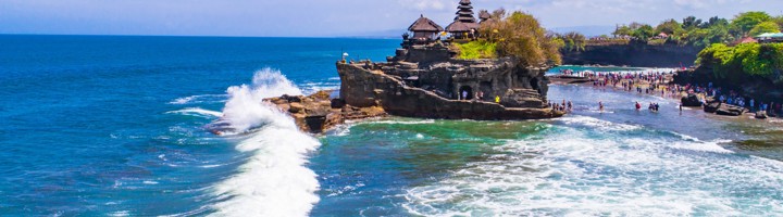 Pura Tanah Lot, tempel op een rots in zee bij Bali, met golven en bezoekers langs de kust.