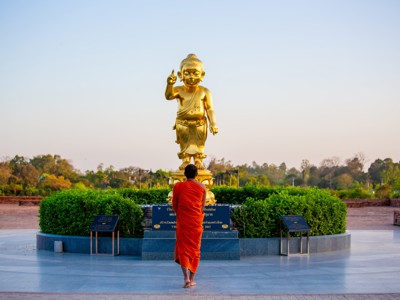 Boeddhistische monnik bij gouden Boeddhabeeld in Lumbini, Route India en Nepal.