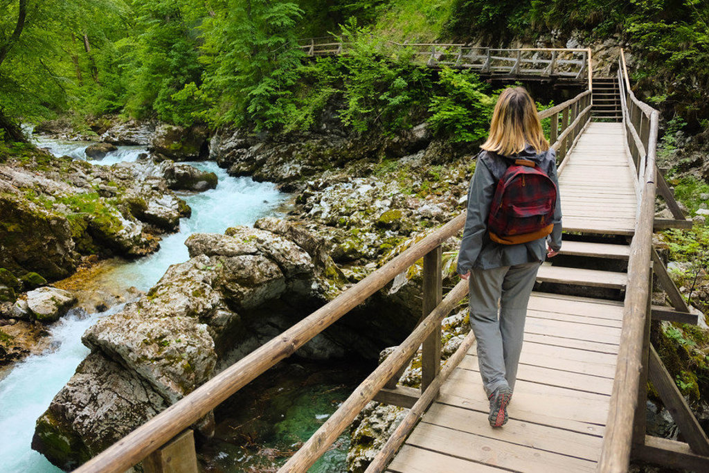 Wandelaar op houten brug langs turquoise rivier in een groene kloof tijdens groepsrondreis Slovenië.