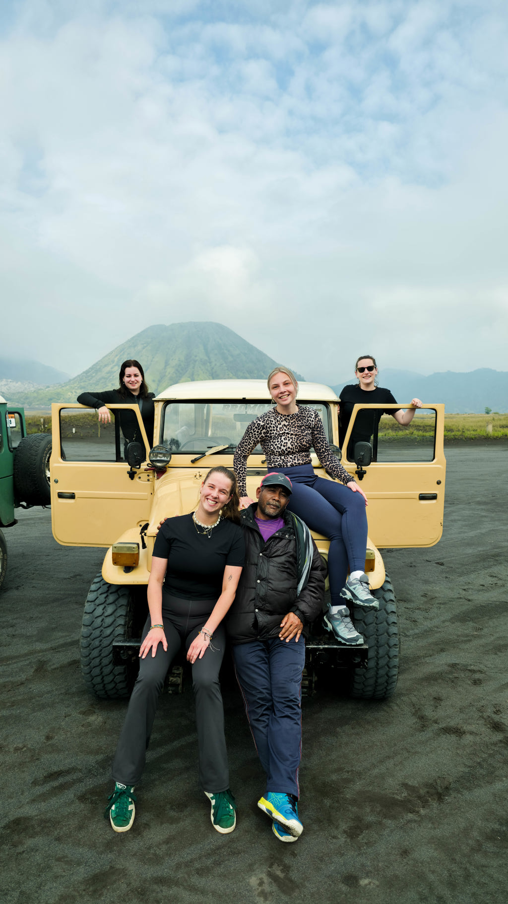 Reisgroep bij een jeep op zwart zand met vulkaan op de achtergrond tijdens 22-35ers reis Indonesië Java en Bali.