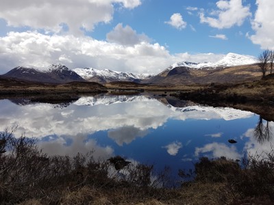 Besneeuwde Schotse Hooglanden weerspiegeld in een stil loch onder een blauwe lucht met wolken.