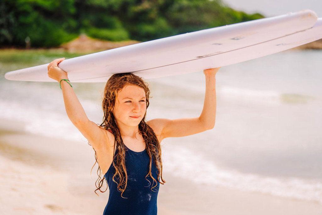 Meisje met surfboard op het strand tijdens familiereis Thailand.