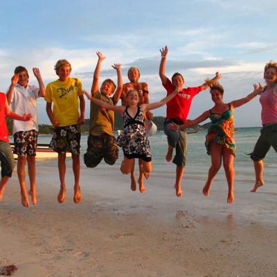 Gezin springt juichend op het strand tijdens familiereis Thailand, Laos en Cambodja.