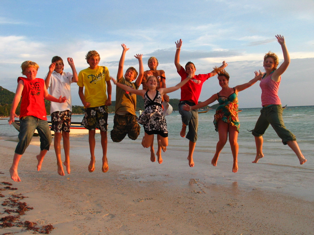 Gezin springt juichend op het strand tijdens familiereis Thailand, Laos en Cambodja.