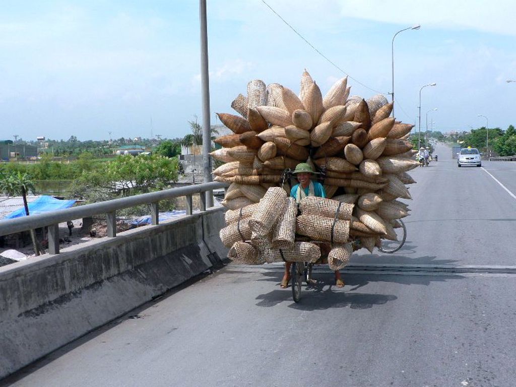 Fietser in Vietnam met enorme lading rieten manden op een brug tijdens groepsrondreis Vietnam kort.