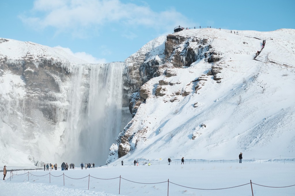 Skógafoss-waterval in de winter, met besneeuwde kliffen en bezoekers in IJsland.