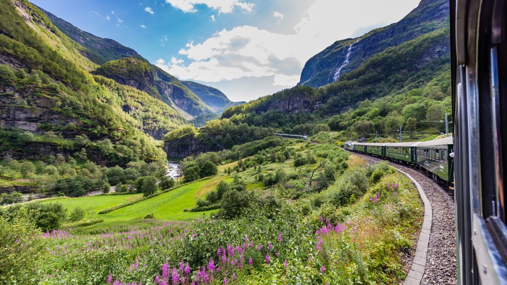 Treinreis door groene bergen en dalen in Scandinavië, met uitzicht op rivier en waterval.