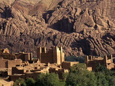 Kasbah in de Atlasbergen langs de Route Marokko, omringd door rotsformaties en palmbomen.