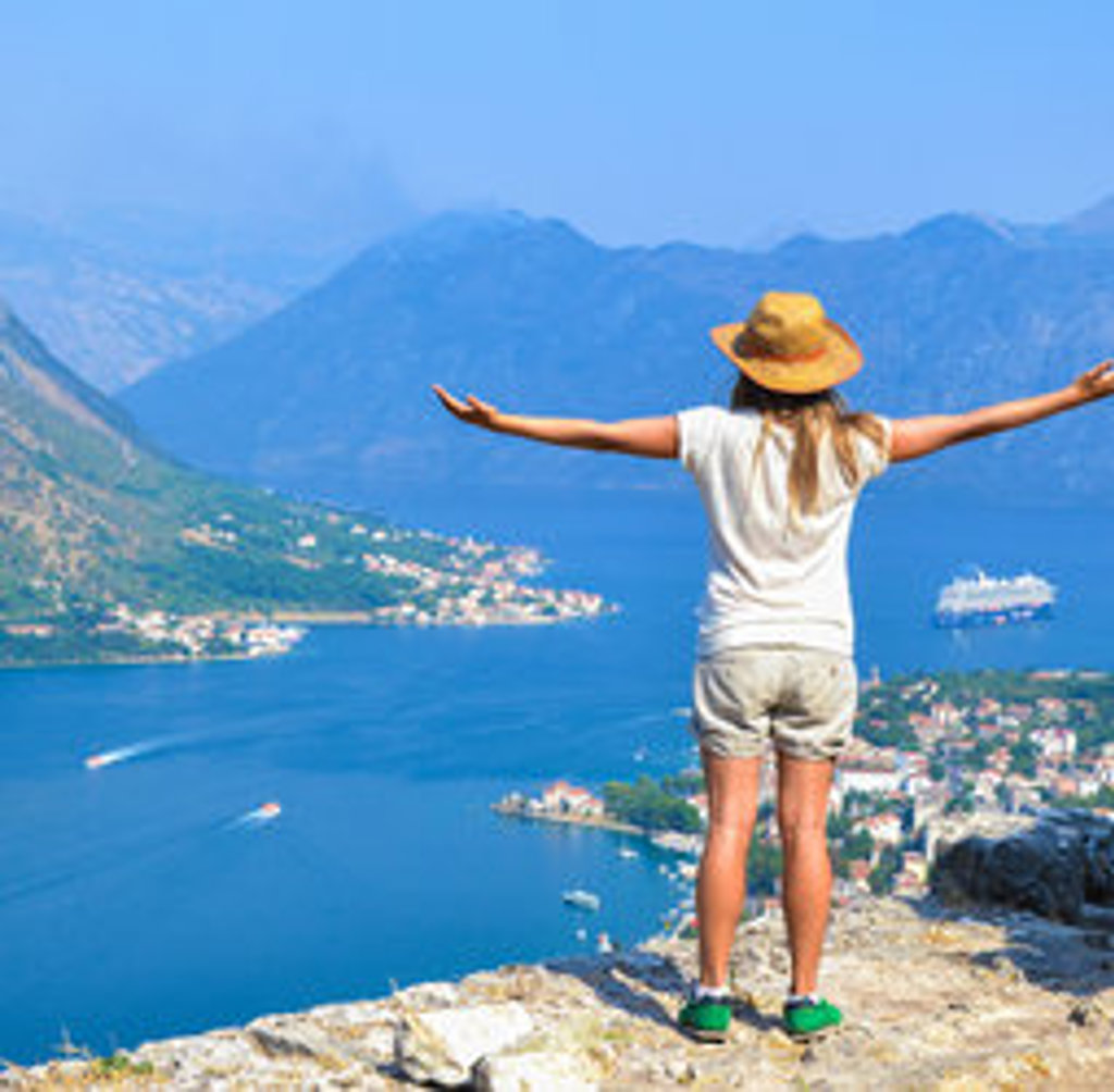 Jonge reiziger met hoed kijkt uit over de Baai van Kotor in Montenegro, met bergen en kustplaatsjes.