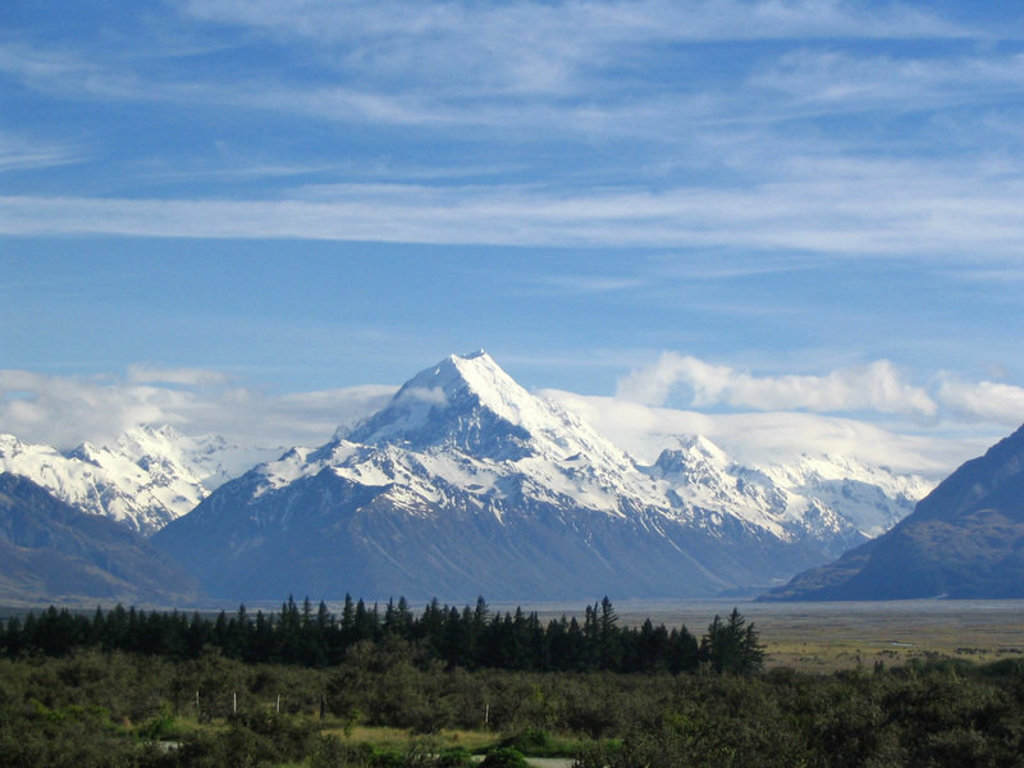 Sneeuwtoppen van Mount Cook in Nieuw-Zeeland, met uitgestrekte vallei en blauwe lucht.