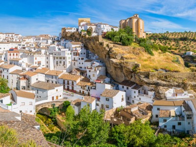 Wit Andalusisch dorp op een rots met kerk en olijfgaarden onder een blauwe lucht.