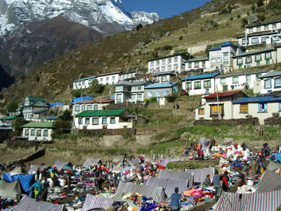 Markt met kleurrijke kramen in Namche Bazaar op de Everest Base Camp-route, met bergdorp en besneeuwde toppen.