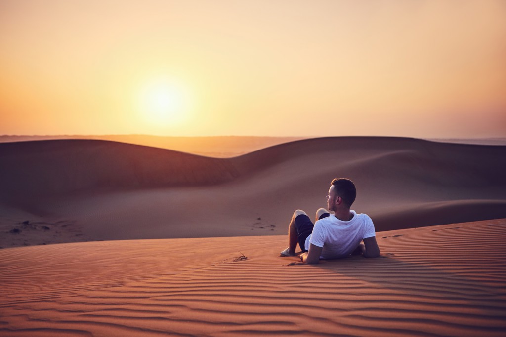 Man kijkt naar de zonsondergang boven de zandduinen in de woestijn tijdens een groepsrondreis Oman en Dubai.