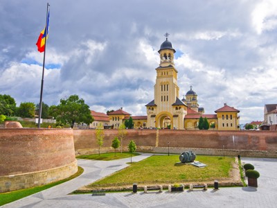 Vestingsmuren en kathedraal van Alba Iulia in Roemenië, met Roemeense vlag onder een bewolkte lucht.