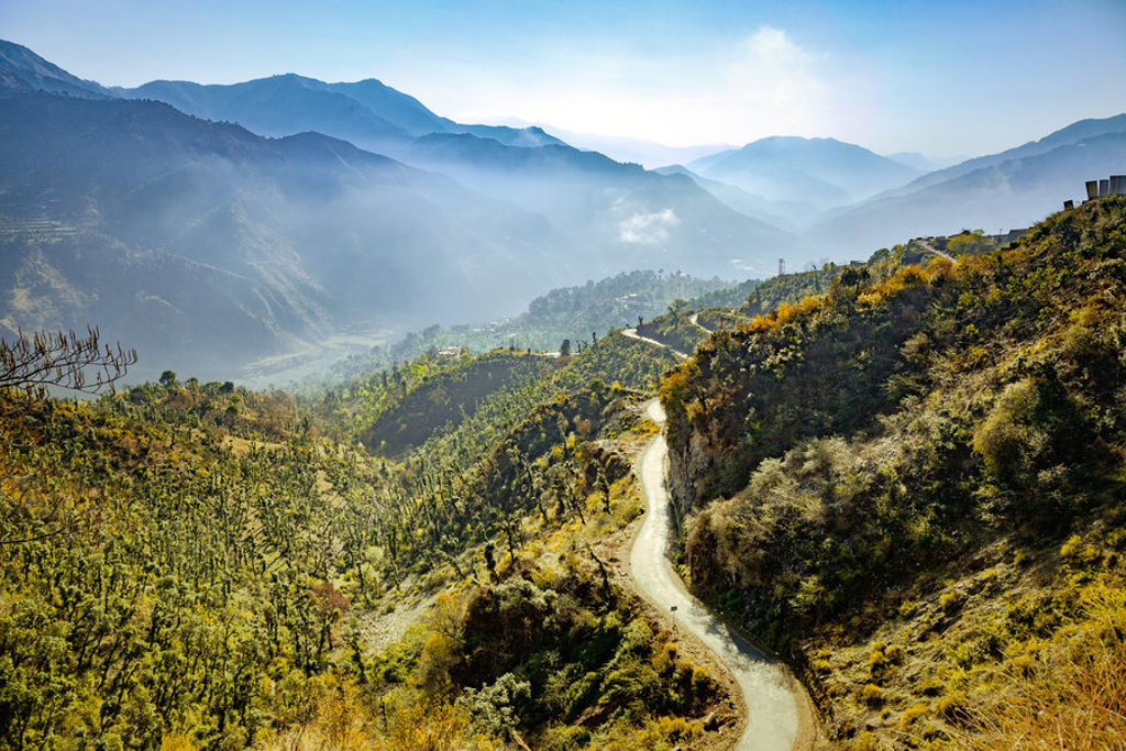 Bochtige bergweg door groene heuvels met mistige bergketens in de verte, Ladakh.