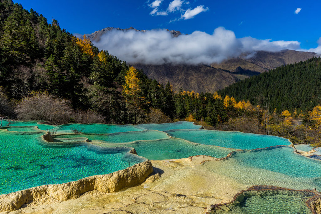 Turquoise kalkterrassen met berglandschap en naaldbos tijdens groepsrondreis China.