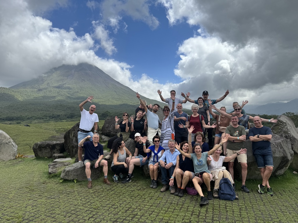 Groepsrondreis Costa Rica: reizigers poseren bij de Arenal-vulkaan, met groene hellingen en wolkenlucht.