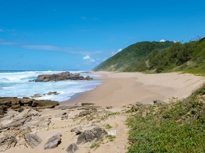 Zandstrand met rotsen en groene duinen langs de kust van Zuid-Afrika.