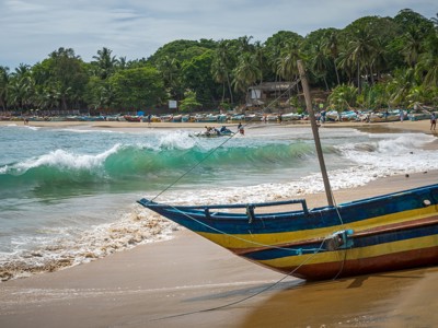 Kleurrijke vissersboot op het strand aan de kust van Sri Lanka, met palmbomen en golven op de achtergrond.