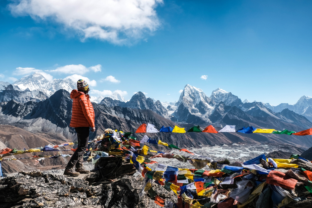 Wandelaar bij kleurrijke gebedsvlaggen met uitzicht op de Himalaya tijdens groepsrondreis Nepal Everest.