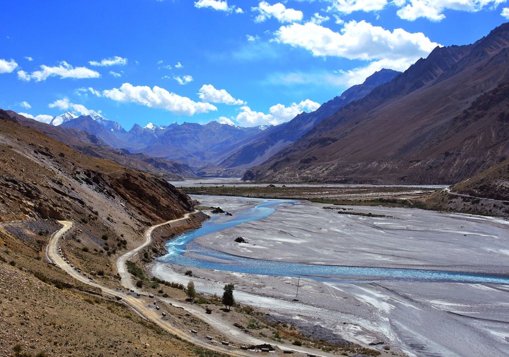 Berglandschap in Ladakh met slingerende weg langs een brede rivierbedding onder een blauwe lucht.
