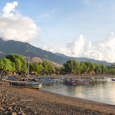Strand met traditionele vissersboten en bergen op de achtergrond tijdens groepsrondreis Java & Bali.