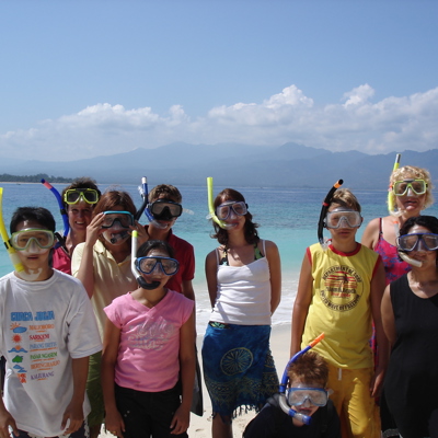 Familiegroep met snorkelmaskers op het strand bij helderblauw water tijdens familiereis Sumatra, Java en Bali.