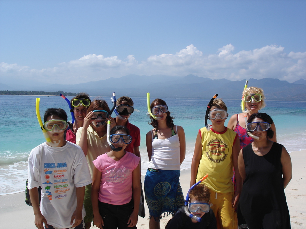 Familiegroep met snorkelmaskers op het strand bij helderblauw water tijdens familiereis Sumatra, Java en Bali.