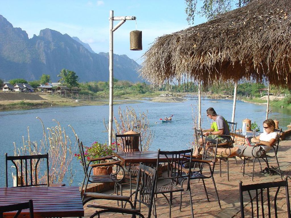 Terras aan de Mekong in Laos met rieten dak, zitplaatsen en uitzicht op rivier en bergen.