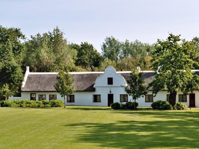Witte Kaaps-Hollandse boerderij met rieten dak tussen bomen, op de route Johannesburg - Kaapstad.