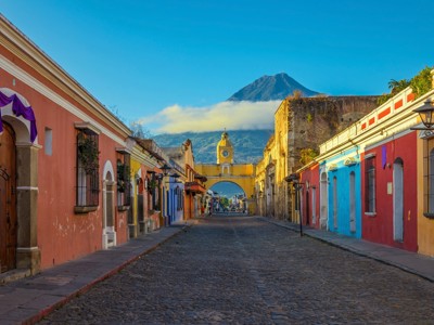 Kleurrijke straat in Antigua Guatemala met de Santa Catalina-boog en de Agua-vulkaan op de achtergrond.