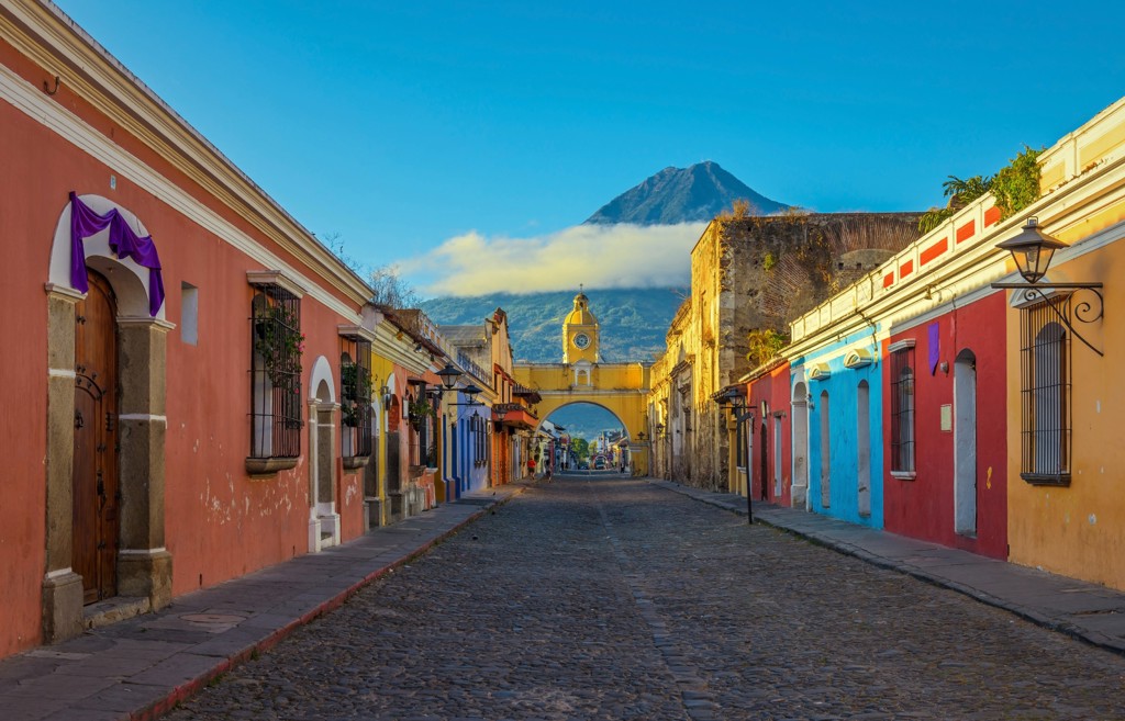 Kleurrijke straat in Antigua Guatemala met de Santa Catalina-boog en de Agua-vulkaan op de achtergrond.